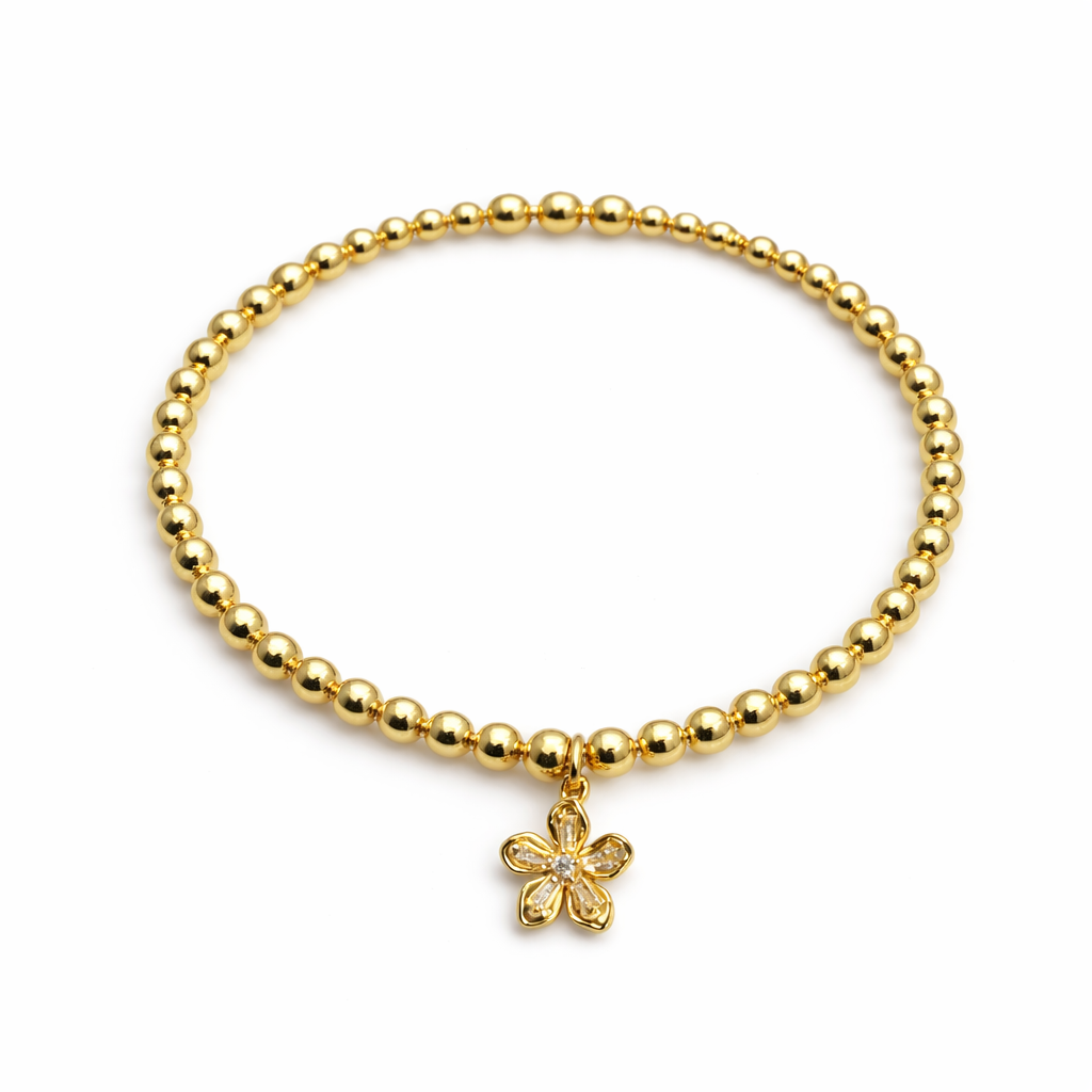 Gold beaded bracelet with a flower charm on a white background