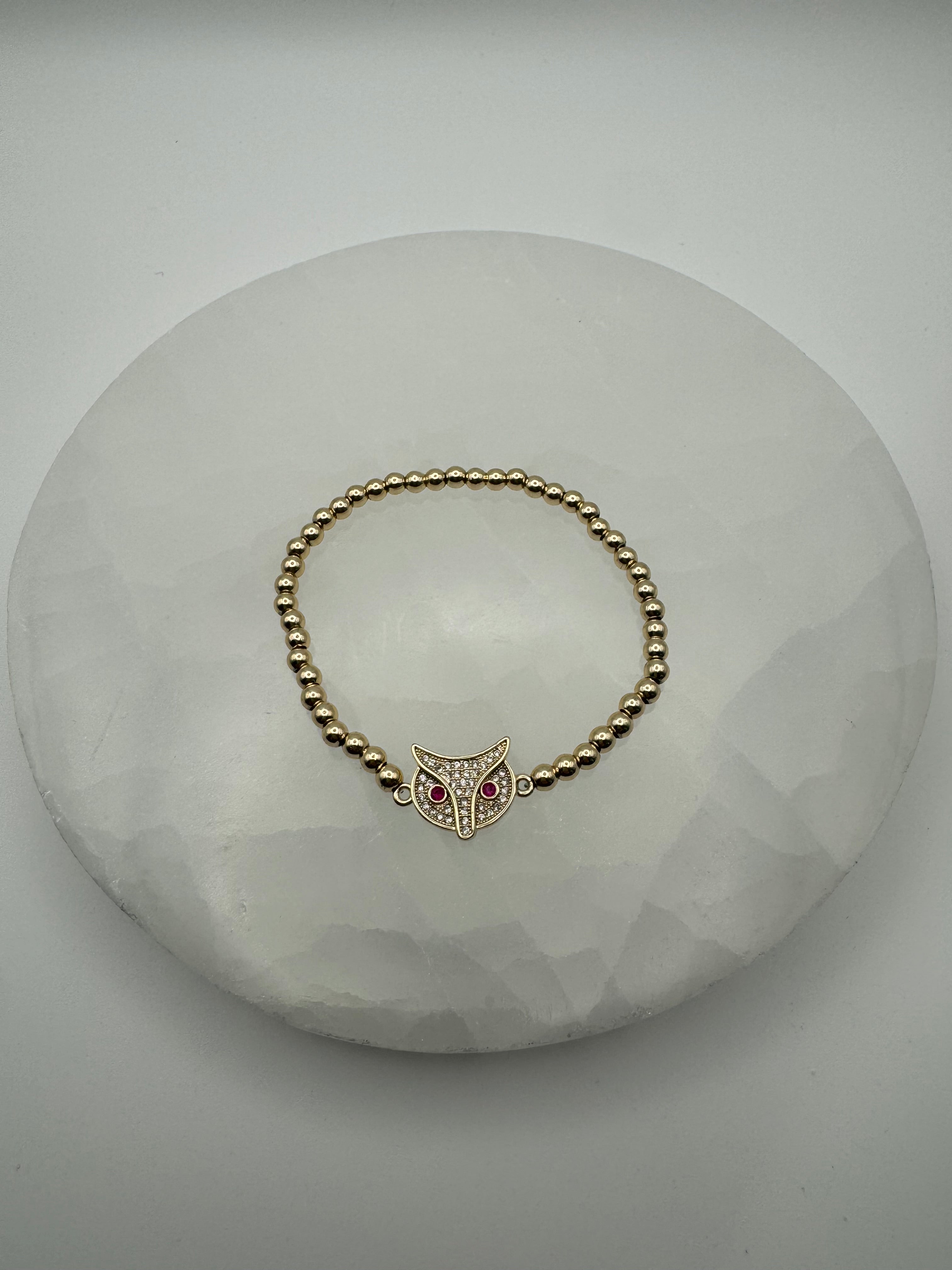 old plated 4mm stretch beaded bracelet with fox owl flat charm on stone surface