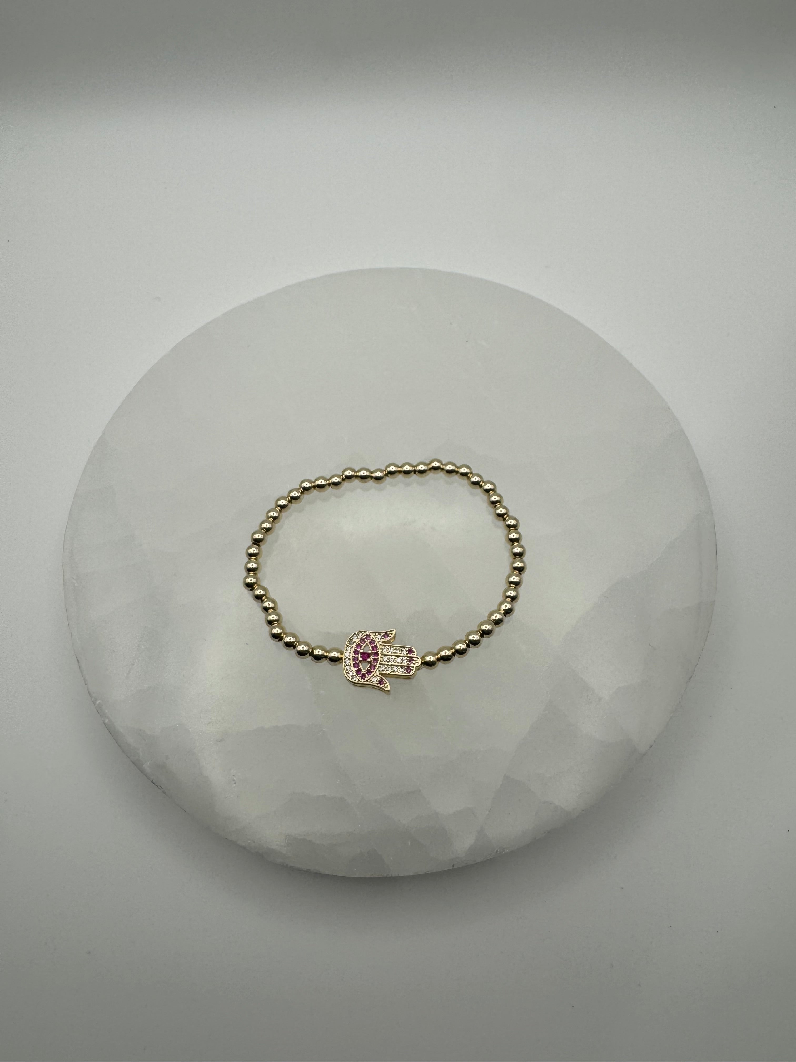 Gold plated 4mm stretch beaded bracelet with hamsa flat charm on stone surface