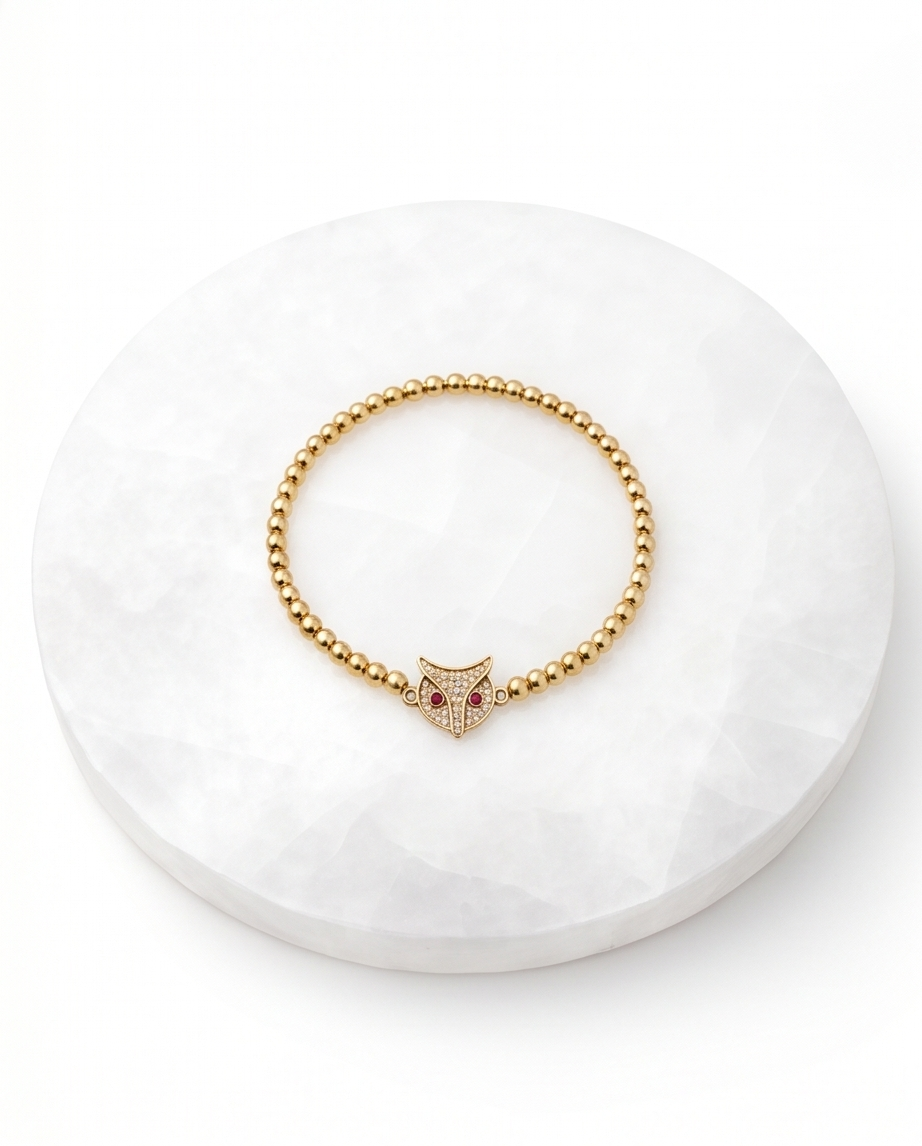 Gold beaded bracelet with owl charm on white stone surface — Stacked by Jayneebell