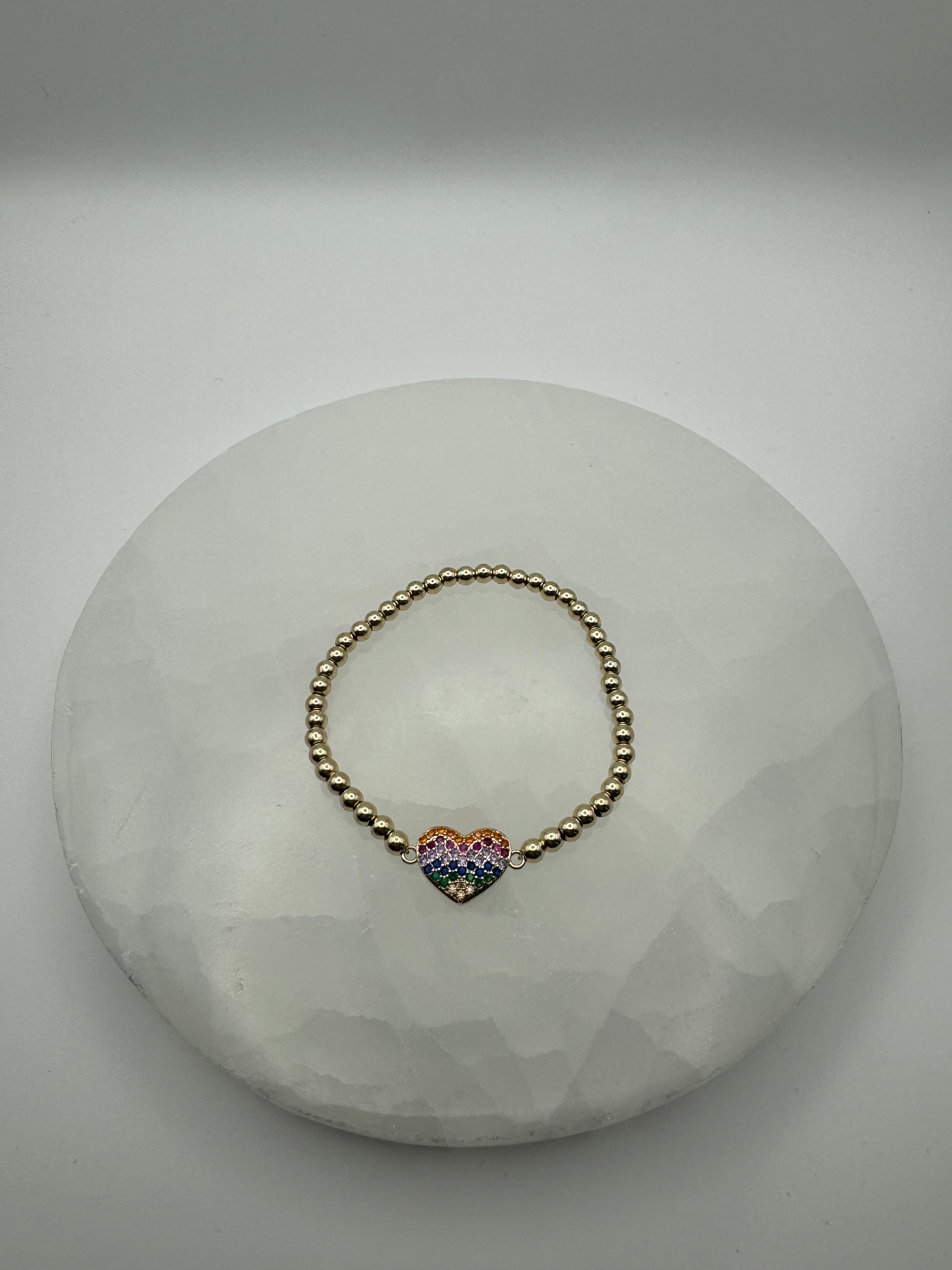 Gold plated 4mm stretch beaded bracelet with rainbow heart flat charm on stone surface