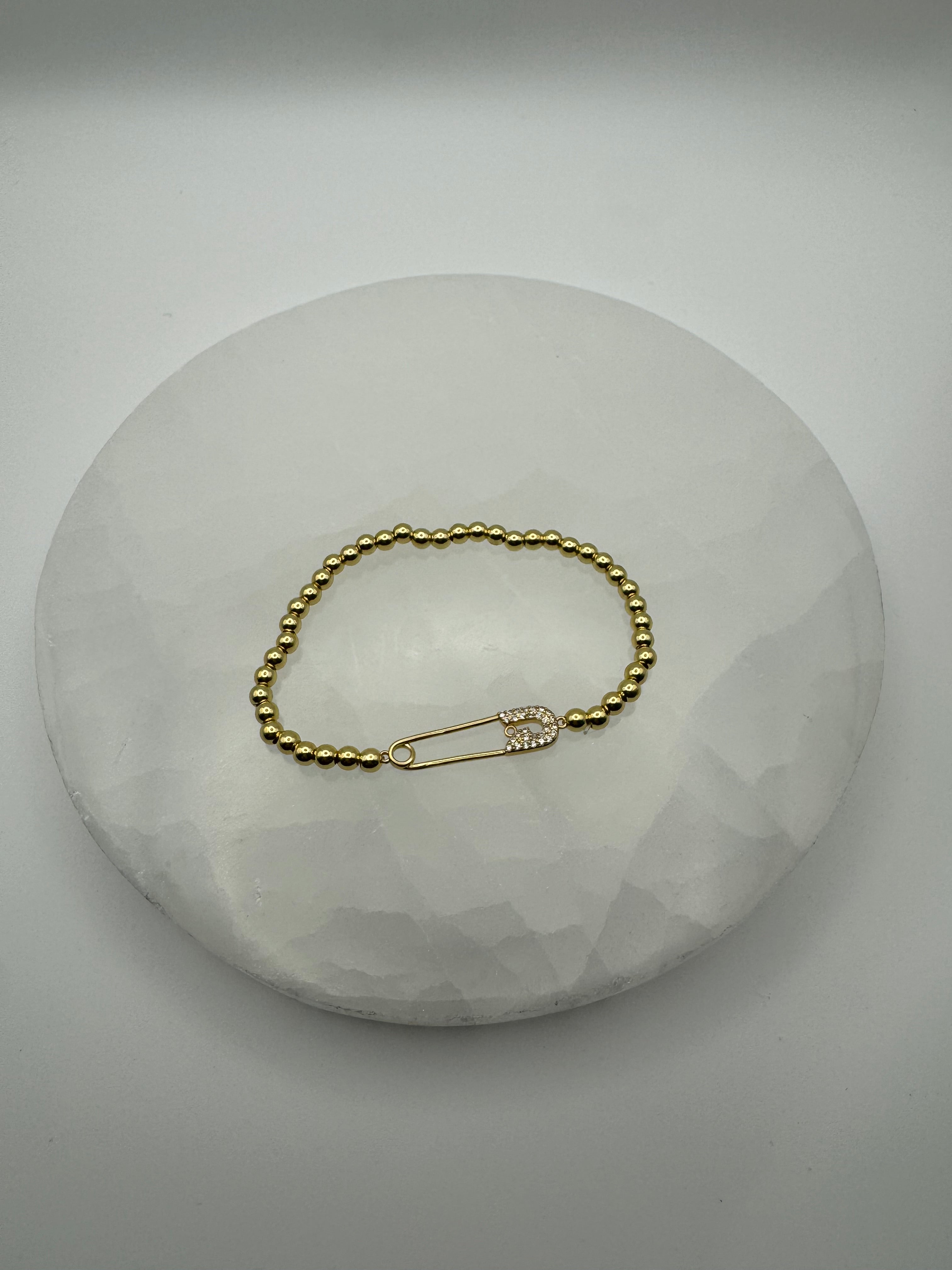 Gold plated 4mm stretch beaded bracelet with safety pin flat charm on stone surface