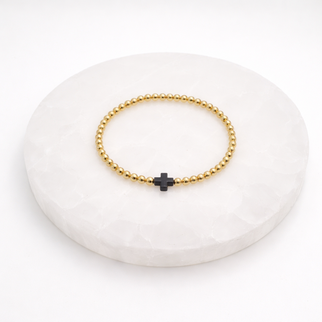 gold beaded bracelet with black resin cross on white background