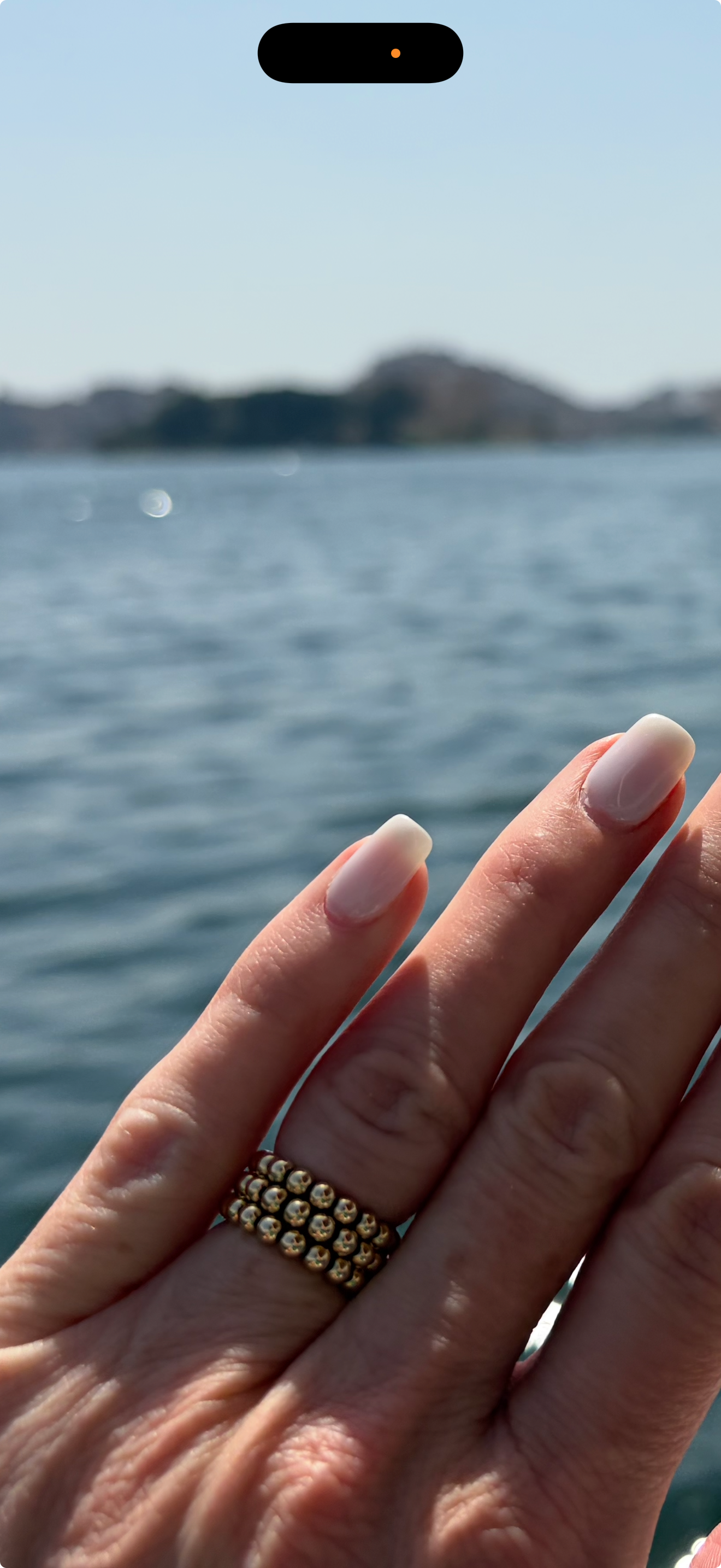 Hand wearing a gold ring with a blurred water background