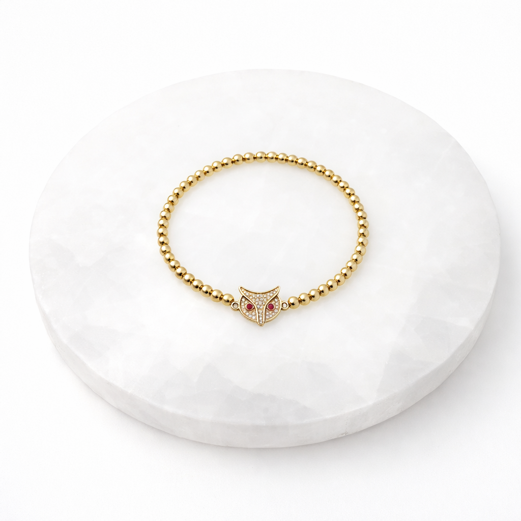 Gold bracelet with owl charm on a white stone surface