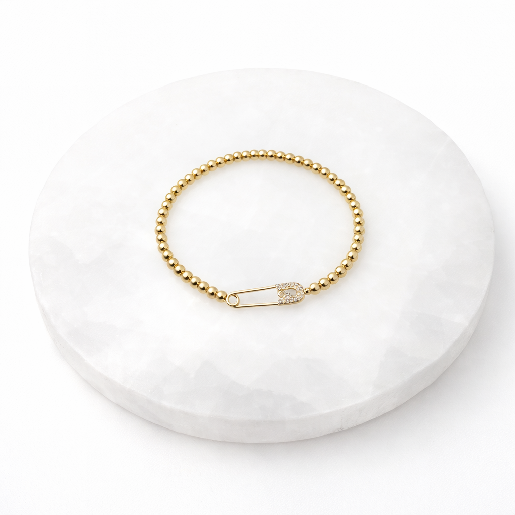 Gold bracelet with a safety pin clasp on a white stone surface