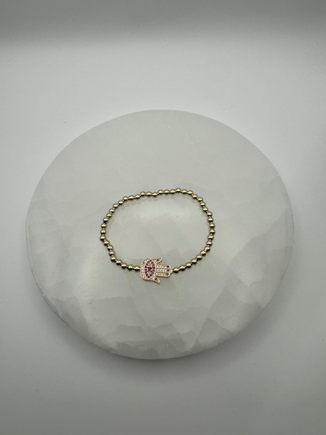 Gold plated 4mm stretch beaded bracelet with hamsa flat charm on stone surface