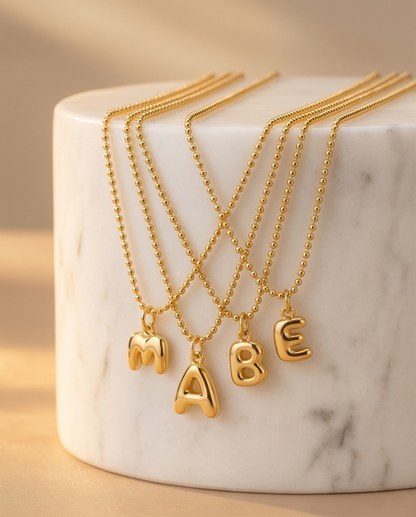 Multiple gold filled bubble initial necklaces with letters M A B E on marble riser — Stacked by Jayneebell
