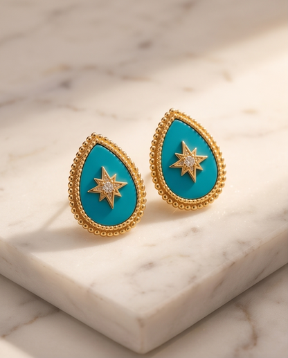 Teardrop-shaped earrings with turquoise stones and gold accents on a marble surface