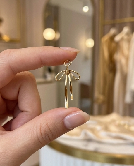  Hand holding gold filled bow charm with trailing ribbon tails in boutique setting — Stacked by Jayneebell