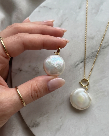 Hand holding freshwater coin pearl pendant beside pearl on gold chain on marble — Stacked by Jayneebell