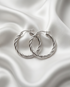 The Rope chunky twisted PVD hoop earrings in silver on white satin fabric, Stacked by Jayneebell