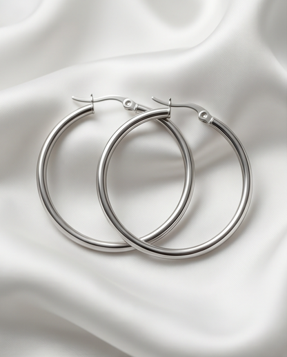 The Silver Standard chunky silver PVD tube hoop earrings on white satin fabric, Stacked by Jayneebell