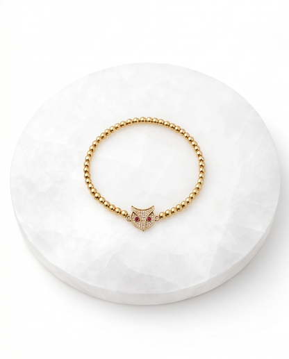 Gold beaded bracelet with owl charm on white stone surface — Stacked by Jayneebell