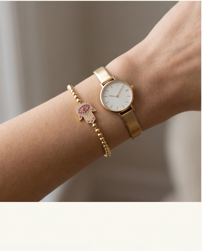 Gold watch and bracelet on a wrist with a blurred background.The Hamsa bracelet styled on wrist with stack — Stacked by Jayneebell