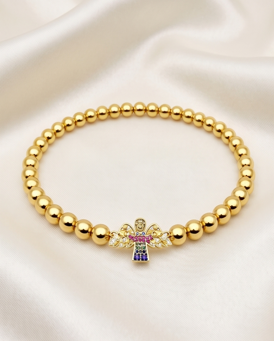 Gold beaded bracelet with a colorful cross charm on a white fabric background. 14k gold plated angel charm stretch bracelet with multicolor CZ flat lay — Heaven Sent by Stacked by Jayneebell