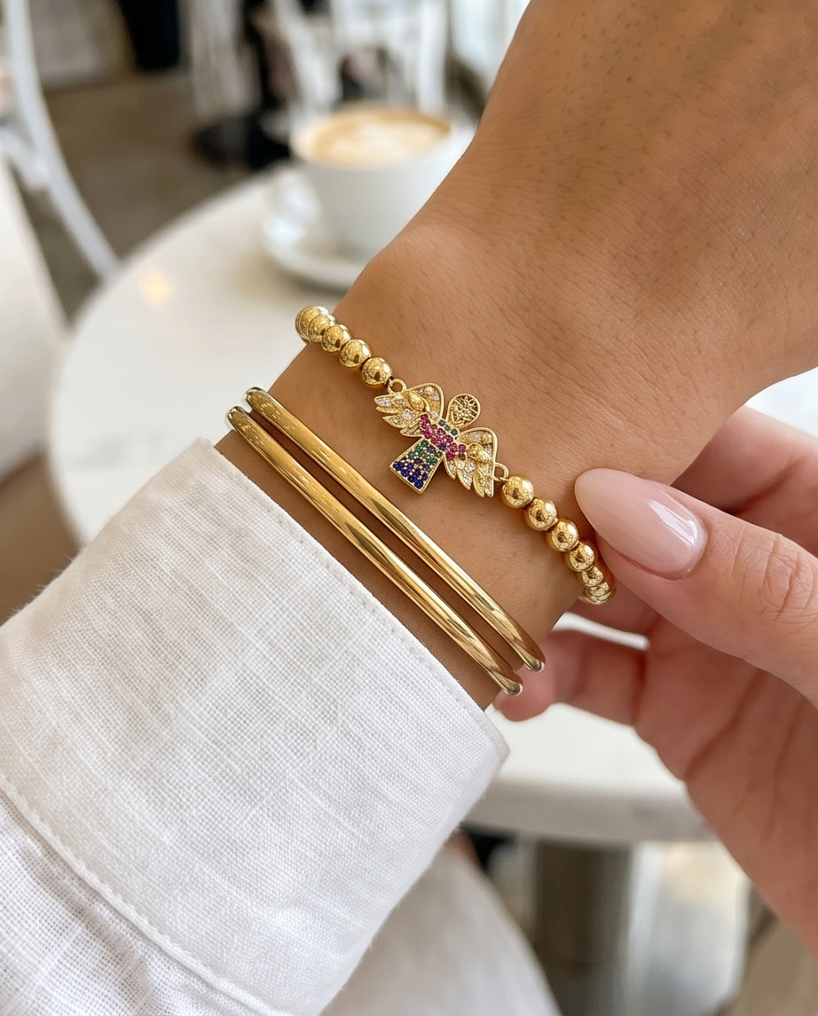 Close-up of a wrist wearing gold bracelets with a blurred indoor background. Gold plated angel charm bracelet styled on wrist — Heaven Sent by Stacked by Jayneebell