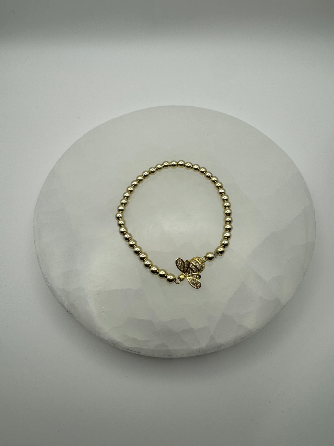 Gold plated 4mm stretch beaded bracelet with signature bee flat charm on stone surface